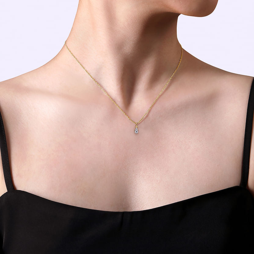 A person wears the Gabriel & Co 14K Yellow Gold Diamond Bujukan Teardrop Pendant Necklace, styled with a black sleeveless top against a light background.