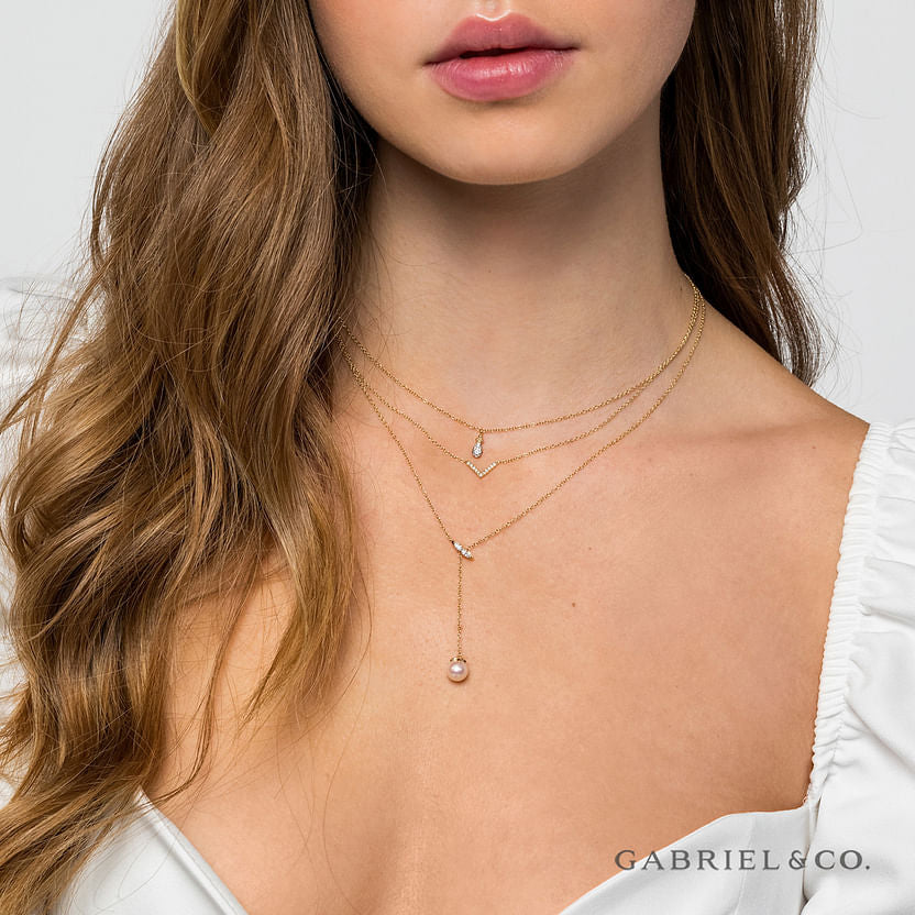 A woman in a white top models three layered gold necklaces, including the Gabriel & Co 14K Yellow Gold Diamond Bujukan Teardrop Pendant Necklace, with diamond and pearl accents. The Gabriel & Co logo is displayed in the bottom right corner.