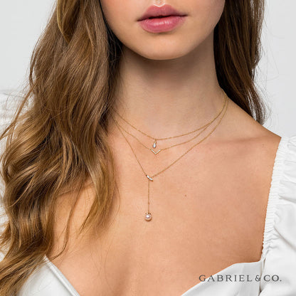 A woman in a white top models three layered gold necklaces, including the Gabriel & Co 14K Yellow Gold Diamond Bujukan Teardrop Pendant Necklace, with diamond and pearl accents. The Gabriel & Co logo is displayed in the bottom right corner.
