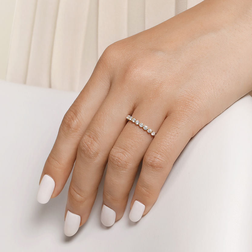 A hand with white-painted nails wears the Gabriel & Co 14K Yellow Gold Diamond Ladies Ring, featuring a row of sparkling natural diamonds. The soft background highlights its stackable luxury and elegant design.