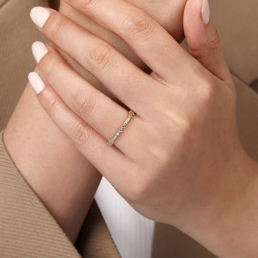 A close-up shows a hand with manicured nails wearing the Gabriel & Co 14K Yellow Gold Diamond Ladies Ring, featuring small natural diamonds, resting gently on the other hand. The person is styled in a beige blazer and white top.