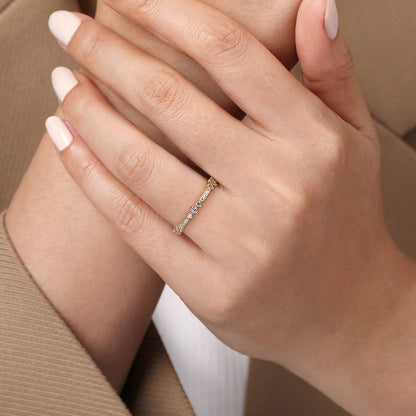 A close-up shows a hand with manicured nails wearing the Gabriel & Co 14K Yellow Gold Diamond Ladies Ring, featuring small natural diamonds, resting gently on the other hand. The person is styled in a beige blazer and white top.