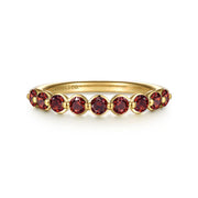The Gabriel & Co 14K Yellow Gold Garnet Stackable Ring features round red gemstones in a continuous prong-set row, with "GABRIEL & CO" engraved inside the band.