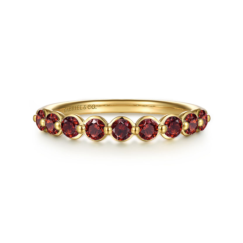 The Gabriel & Co 14K Yellow Gold Garnet Stackable Ring features round red gemstones in a continuous prong-set row, with "GABRIEL & CO" engraved inside the band.