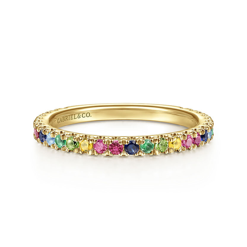 The 14K Yellow Gold Rainbow Color Stone Stackable Ring by Gabriel & Co features a thin band set with small, round blue, green, yellow, and pink gemstones all around, plus an inner engraving of “GABRIEL & CO.”.