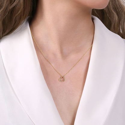 A woman in a white blazer showcases the Gabriel & Co 14K Yellow Gold Tilted Heart Pendant Necklace, featuring a delicate tilted heart resting at the center of her chest.