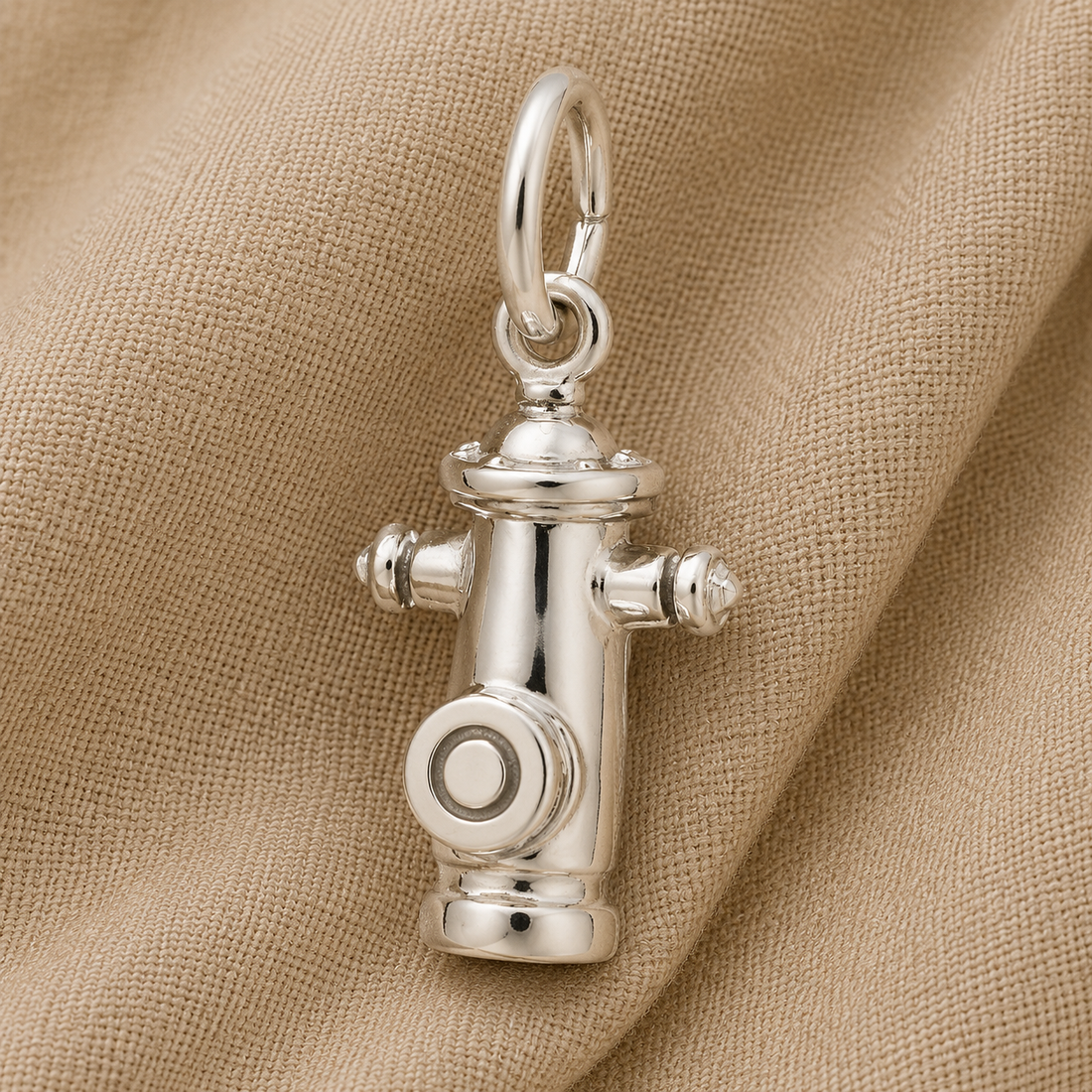 The Rembrandt Charms Fire Hydrant Charm in sterling silver, featuring a loop at the top, rests on a textured beige fabric background—an ideal gift for dog lovers.