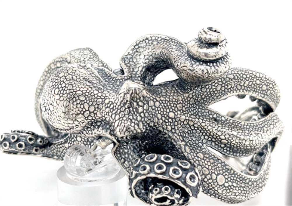 The Kabana SS Large Octopus Bracelet Cuff features textured skin and curled tentacles, displayed as a striking statement piece on a clear stand against a white background.