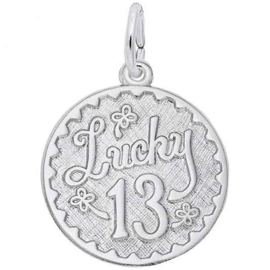 The Lucky 13 Charm by Rembrandt Charms is a sterling silver, round pendant showcasing the word "Lucky" in cursive script above the number "13". The charm features a scalloped edge and is adorned with small flower designs around the text. It includes a small silver loop at the top for hanging.