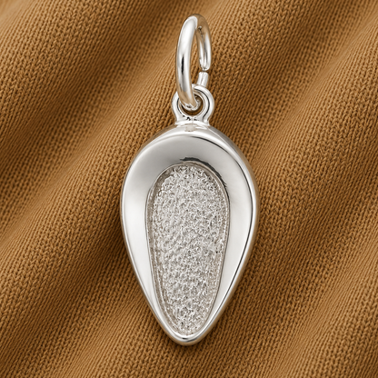 A gleaming sterling silver Bed Pan Charm by Rembrandt Charms, featuring an organic, oval shape with smooth edges and a textured center, rests atop a brown textured fabric background. With its large top loop for easy attachment to a chain, this unique piece makes an ideal healthcare jewelry accessory or thoughtful nurse gift.