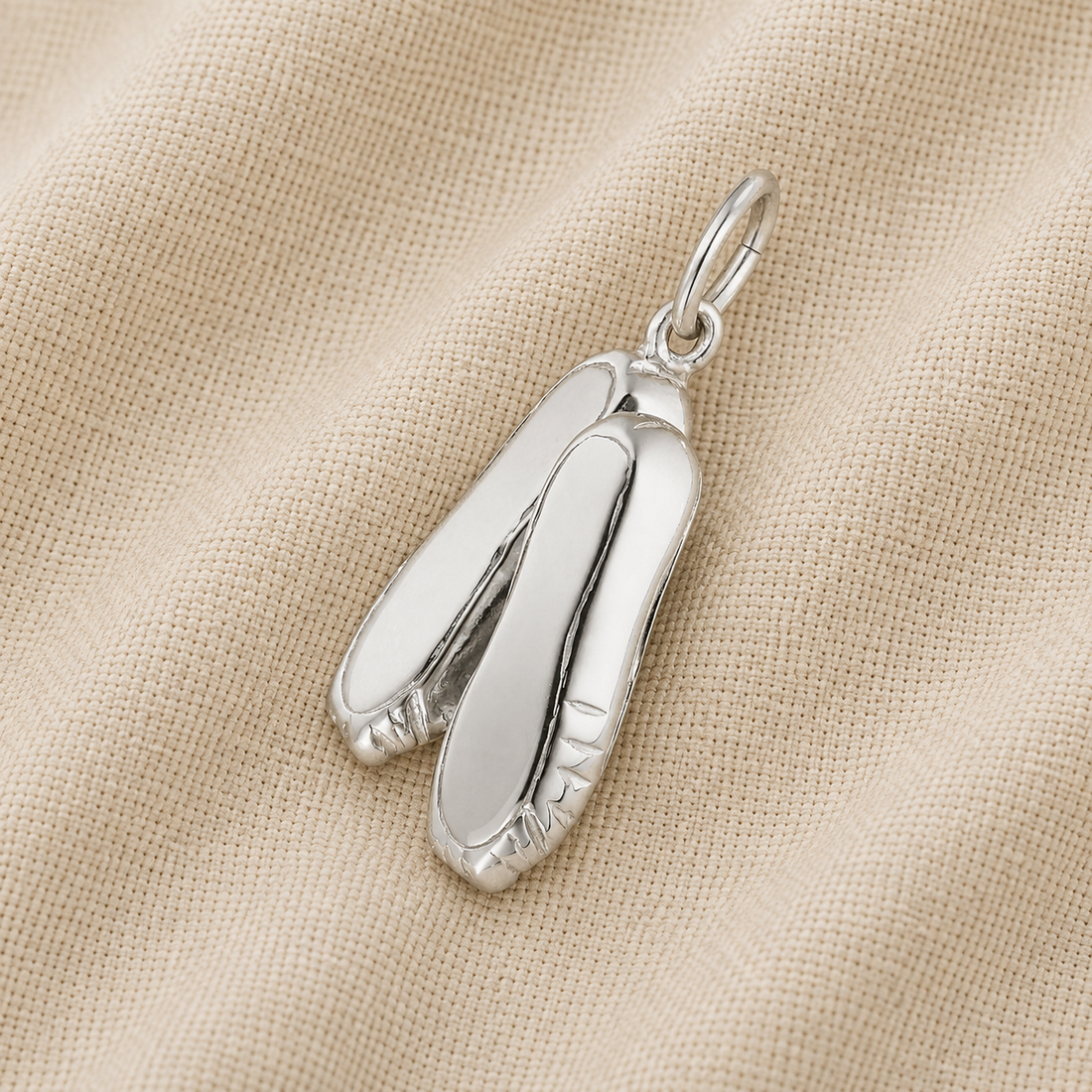A Ballet Shoes -Sterling Silver charm by Rembrandt Charms, ideal as ballet jewelry or a cherished dance keepsake, rests on a textured beige fabric background.