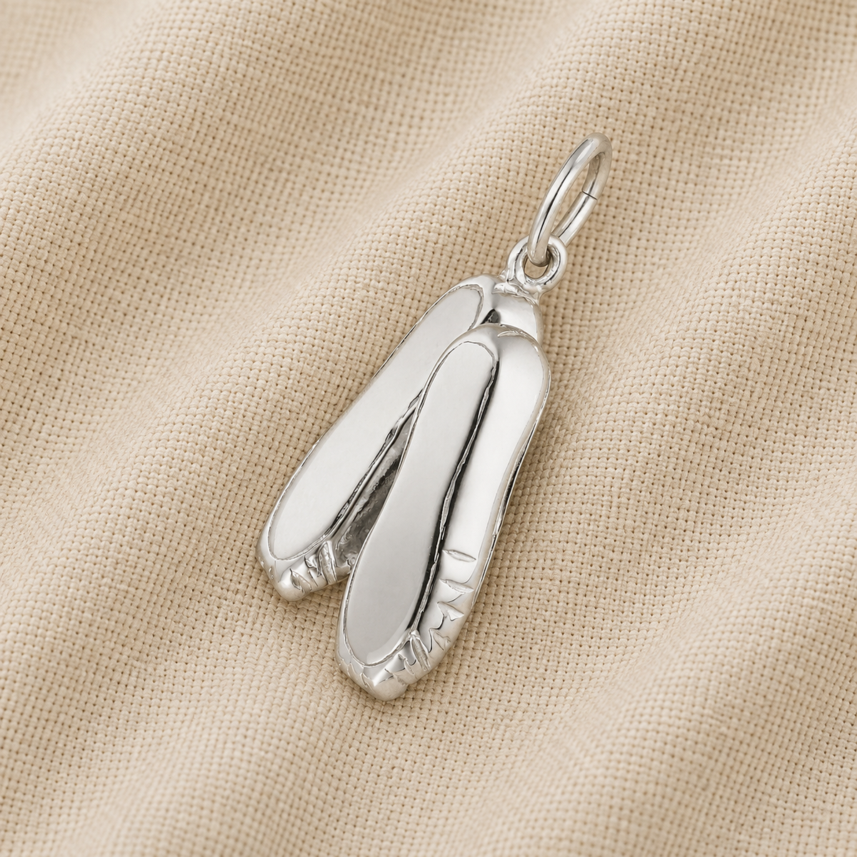 A Ballet Shoes -Sterling Silver charm by Rembrandt Charms, ideal as ballet jewelry or a cherished dance keepsake, rests on a textured beige fabric background.