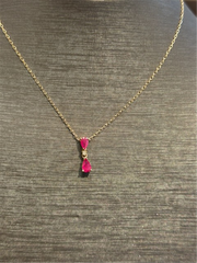 The Ryan Gems Ruby Drop Pendant features two pink rubies—an oval and a teardrop—set on a delicate 14k yellow gold chain, displayed on a gray textured jewelry bust.