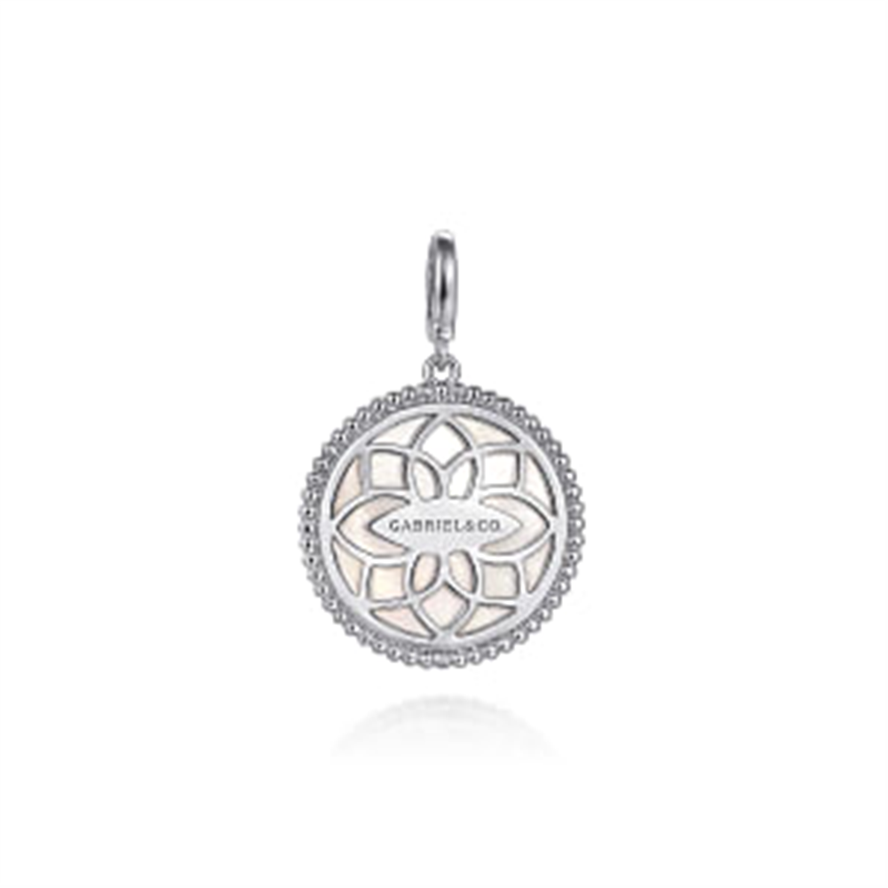 The 925 Sterling Silver Bujukan White Sapphire and Mother Of Pearl Round pendant by Gabriel & Co. features an intricate, floral-like cutout design. Crafted from 925 sterling silver, the pendant has "Gabriel & Co." engraved in the center. The outer edge showcases a textured, beaded pattern, adorned with a delicate white sapphire and includes a small, smooth loop for attaching to a chain.