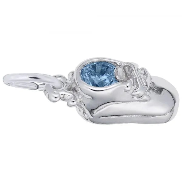 The Rembrandt Charms December Baby Shoe Charm in sterling silver is crafted in the shape of a baby shoe and adorned with intricate details, featuring a blue topaz birthstone at the opening. It includes a loop for attaching to a bracelet or necklace.