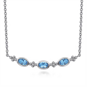 The Gabriel & Co 925 Sterling Silver Bujukan Blue Topaz Bar Necklace (Serial No: S174) features a delicate arrangement of three Swiss Blue Topaz gemstones positioned horizontally. Small silver accents are set between each gemstone, all gracefully displayed on a fine 925 Sterling Silver chain. This exquisite piece embodies the elegance and craftsmanship associated with the Gabriel & Co brand.