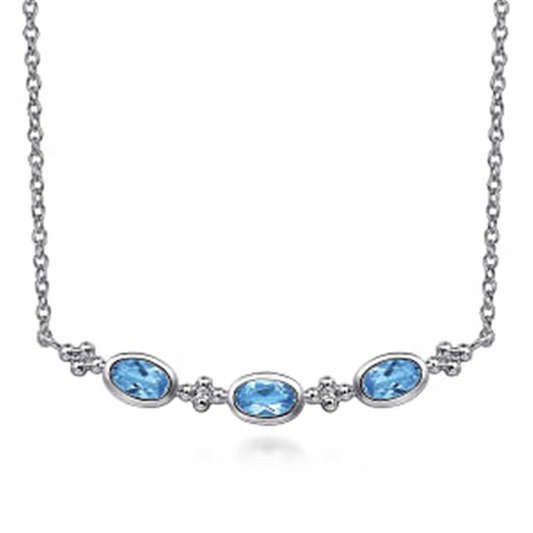 The Gabriel & Co 925 Sterling Silver Bujukan Blue Topaz Bar Necklace (Serial No: S174) features a delicate arrangement of three Swiss Blue Topaz gemstones positioned horizontally. Small silver accents are set between each gemstone, all gracefully displayed on a fine 925 Sterling Silver chain. This exquisite piece embodies the elegance and craftsmanship associated with the Gabriel & Co brand.