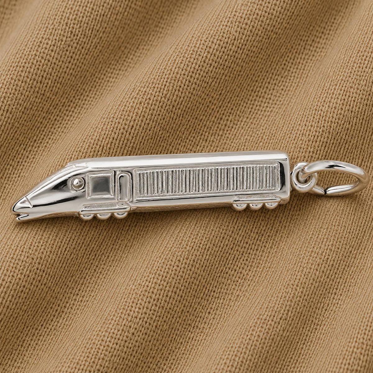The Rembrandt Charms Eurotrain Charm—crafted in sterling silver and featuring detailed windows and wheels—rests on a textured light brown fabric background.
