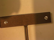 A close-up view of a jewelry piece, likely an earring stand, showcases two small, round, sparkling 0.63ctw stud earrings in a 4-prong setting attached to a horizontal bar. The surface of the bar appears metallic and textured. The background is warmly lit with gold hues reflecting off the Veer 14KW 4-prong / 0.63ctw Stud earrings.
