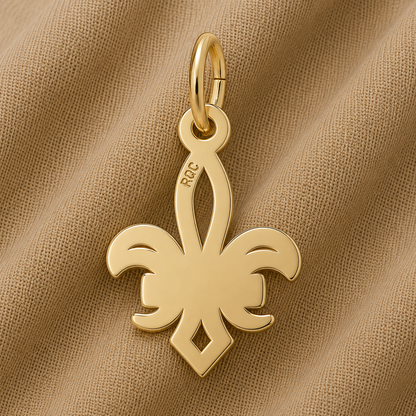 A gold-plated NOLA Fleur de Lis Charm by Rembrandt Charms, featuring a smooth, shiny surface and “RCC” engraved on one side, rests atop tan fabric—a timeless Crescent City keepsake and an elegant piece of New Orleans jewelry.
