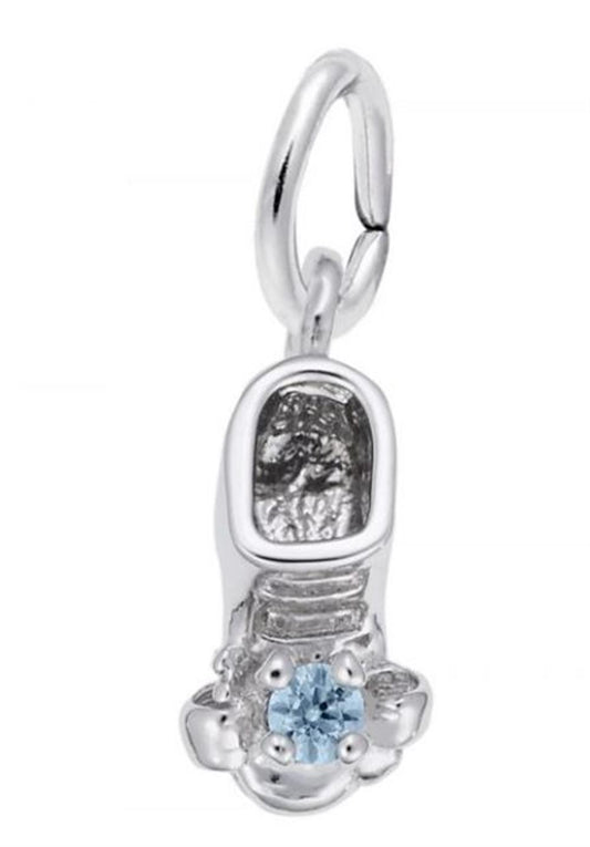 The image shows the Sterling Silver March Baby Shoe Charm from Rembrandt Charms. The charm is crafted in sterling silver and features a detailed baby shoe with an aquamarine-colored stone. It measures 0.2 inches by 0.43 inches (5 mm x 11 mm) and has the style number 2734-003. This charm is a perfect keepsake for commemorating the birth of a March baby.