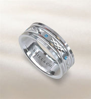 The Gabriel & Co mens silver and blue topaz ring features engraved geometric patterns and blue gemstones, with "GABRIEL & CO." inscribed inside. This stylish accessory is set against a soft, light beige background.