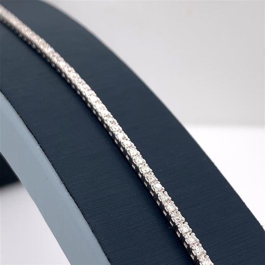 A luxurious display features the 1.0000 Ctw Diamond Tennis Bracelet by SDC Creations-SDC, a stunning 14 kt silver piece adorned with a row of sparkling diamonds, positioned diagonally against a sleek, dark blue and light gray rounded backdrop. The elegant design highlights the brilliance and clarity of the diamonds, showcasing its sophisticated allure.