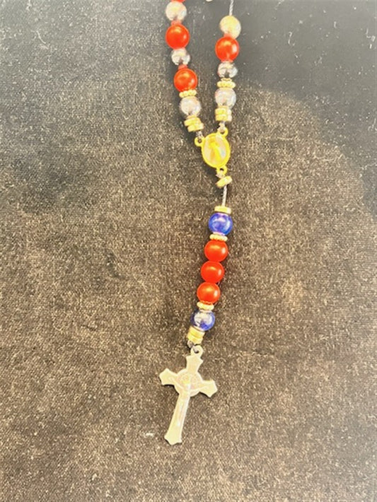 The SR002 Small Red Jasper, Blue Tiger Eye, & Hematite Rosary by Redemption Jewelry is displayed on a dark, textured surface, featuring rich beads and a silver cross pendant.