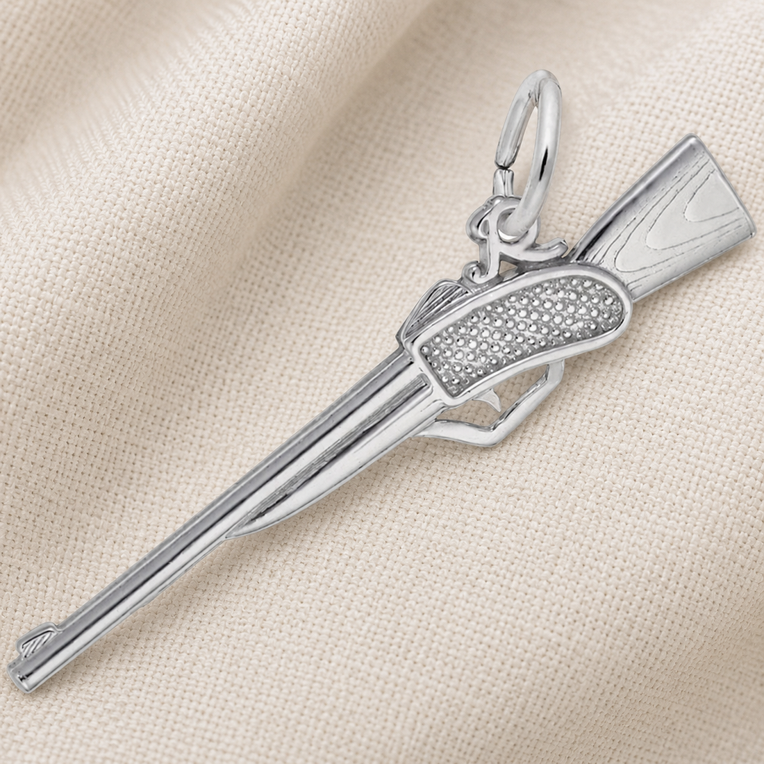 A sterling silver Rifle Charm by Rembrandt Charms, featuring a detailed textured grip, rests on a beige textured fabric background—making it an ideal hunting gift or a unique accessory for shooting-sports enthusiasts.