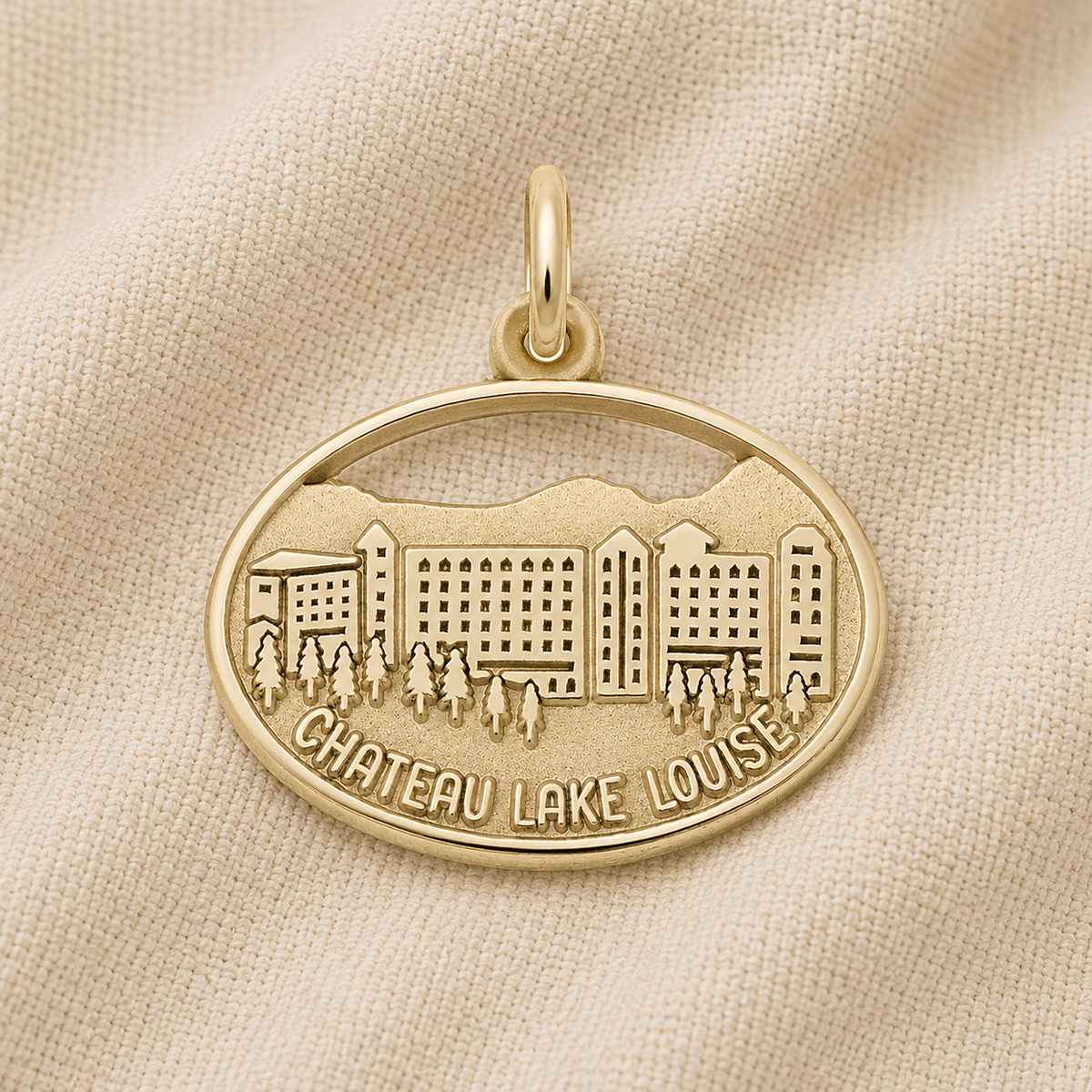 The Chateau Lake Louise - Gold Plated Charm by Rembrandt Charms features an elegant engraving of a building, mountains, trees, and the words “Chateau Lake Louise.” Resting on a beige fabric background, this timeless charm is the perfect Alberta keepsake, capturing the spirit of the Canadian Rockies in classic style.