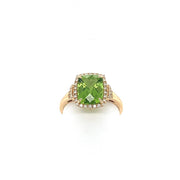 The Peridot and Diamonds Ring by Bellarri features a 14K yellow gold band with a large, rectangular peridot at the center, surrounded by small clear diamonds. The band showcases an elegantly designed, intricate pattern, all displayed against a plain white background.