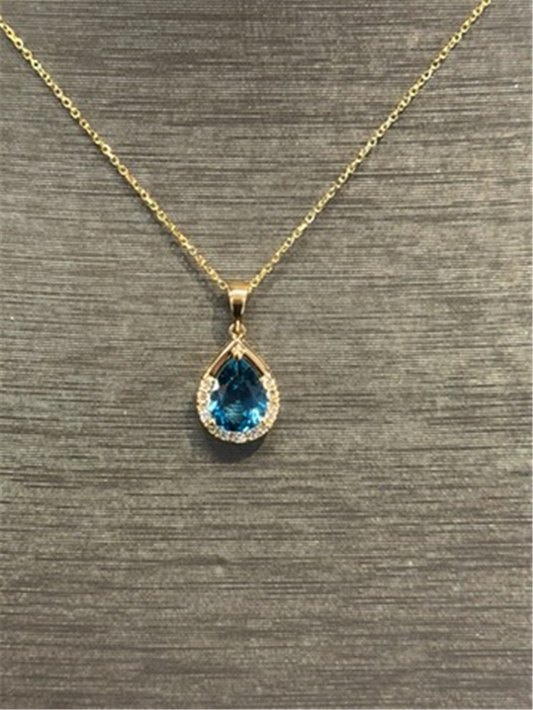 The Ryan Gems London Blue Topaz Pear Shaped Pendant in 14k yellow gold features a pear-shaped blue topaz surrounded by clear stones, showcased on a textured gray background.