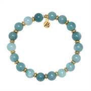 Part of the T Jazelle Gold Empowered Elegance Collection, the Mountain Blue Jade Gemstone Bracelet features round blue-green stones, gold spacers, and an engraved gold charm arranged in a circle on a white background.