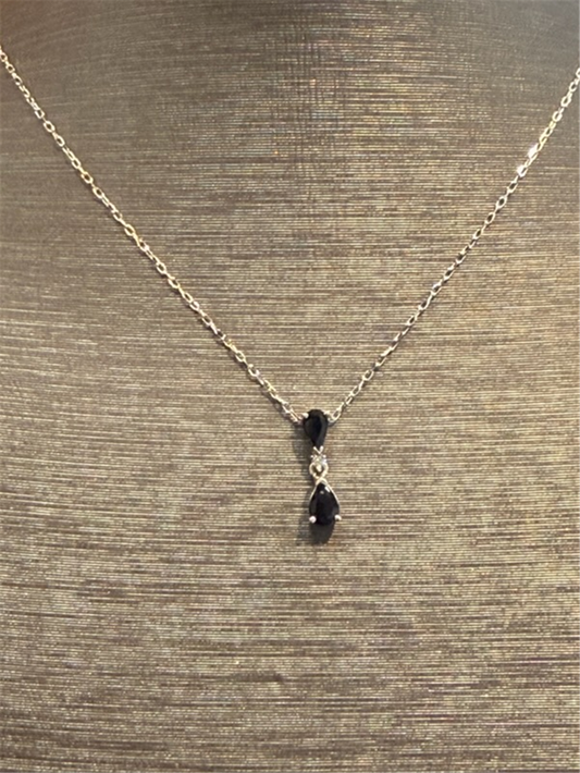 The Pear Shaped Sapphire Drop Pendant by Ryan Gems features two black pear-shaped stones vertically connected by a clear stone on a 14k white gold chain, elegantly displayed on a textured beige bust.