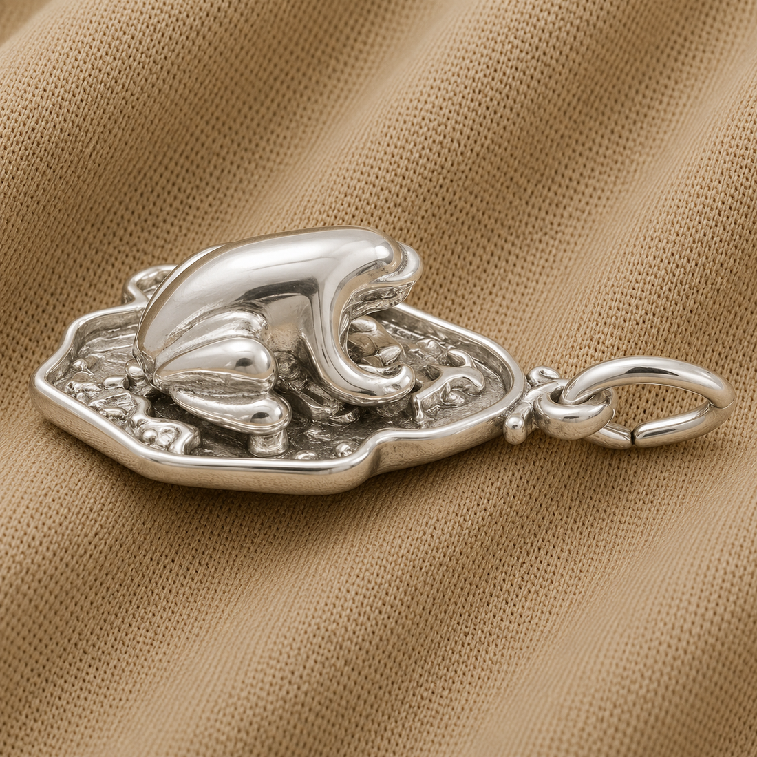 A Frog on Lily Pad Charm by Rembrandt Charms in sterling silver rests on a textured beige fabric surface, showcasing intricate detailing and a polished finish—an enchanting addition perfect for introducing whimsical flair to your jewelry collection.