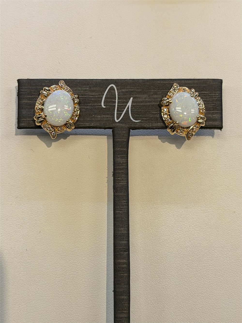 Ryan Gems Diamond and Opal Studs in 14k yellow gold with diamond accents are displayed on a dark stand against a light background.