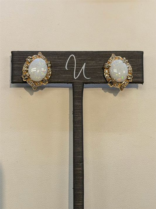 Ryan Gems Diamond and Opal Studs in 14k yellow gold with diamond accents are displayed on a dark stand against a light background.