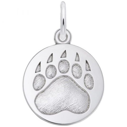 A silver circular pendant from Rembrandt Charms, featuring an engraved bear paw print design, is shown. The Bear Paw Print Charm in Sterling Silver has a glossy finish with textured details on the paw print and a small loop at the top for attaching to a chain or bracelet. It’s perfect for those who cherish wilderness jewelry.