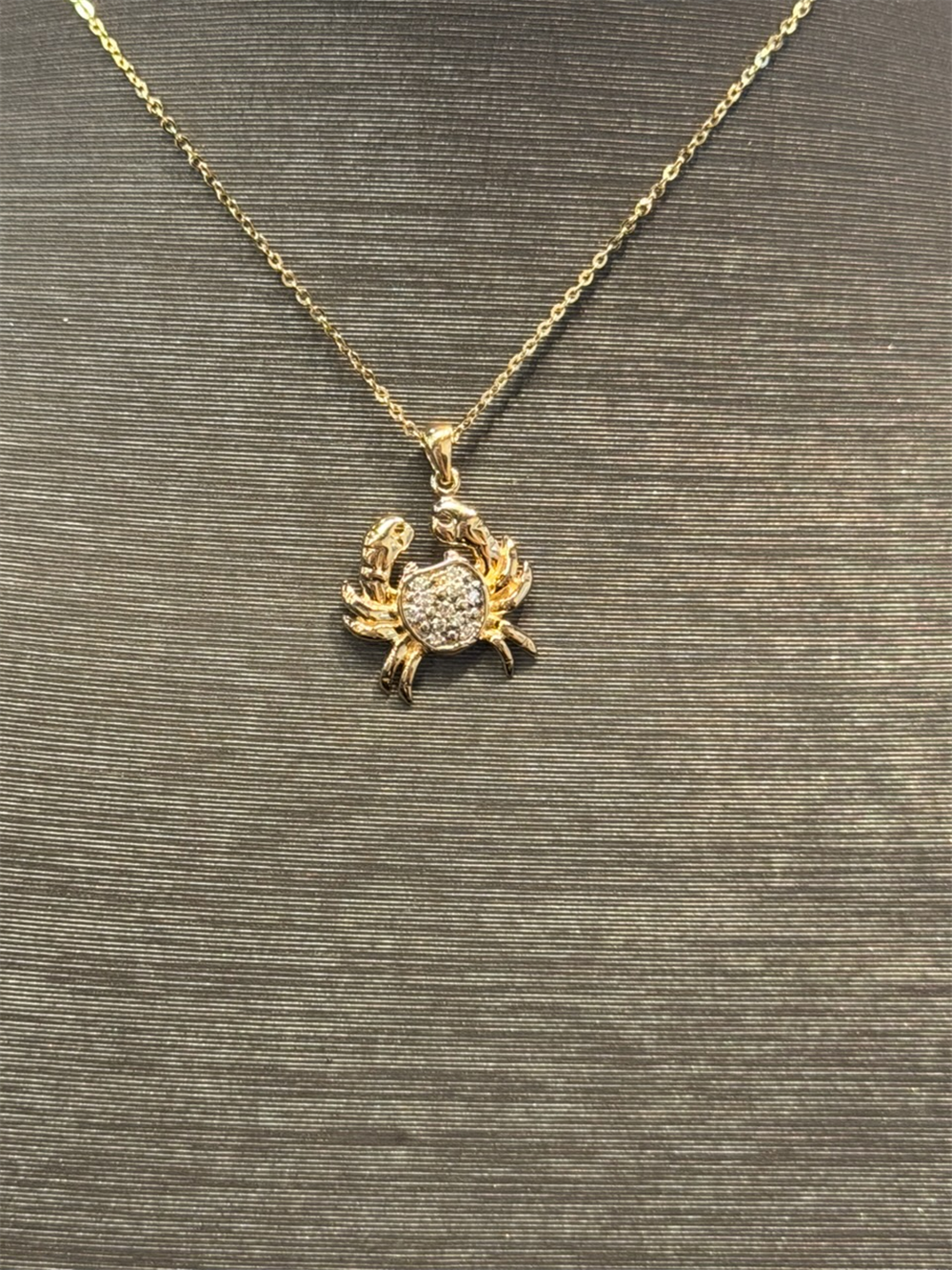The Ryan Gems Diamond Crab Necklace features a 14k yellow gold chain with a crab-shaped pendant adorned with sparkling stones, elegantly displayed against a textured dark background.