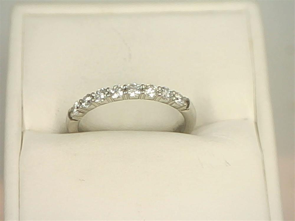 The 14K White Gold .4800ctw Round Cut Diamond Band Ring Shared Prong from Benchmark Rings is elegantly displayed on a cushioned, cream-colored background, featuring a row of seven small lab-grown, round-cut diamonds.