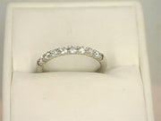 The 14K White Gold .4800ctw Round Cut Diamond Band Ring Shared Prong from Benchmark Rings is elegantly displayed on a cushioned, cream-colored background, featuring a row of seven small lab-grown, round-cut diamonds.