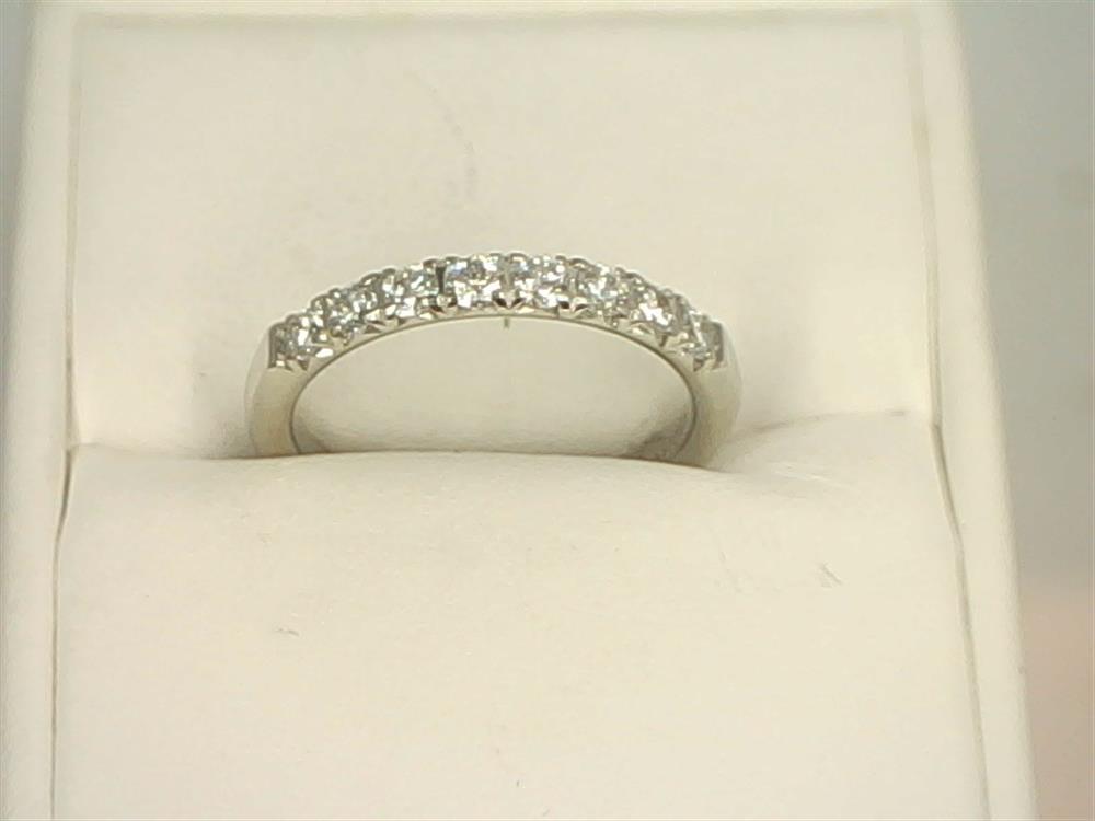 A 14K white gold ring adorned with a row of small, lab-grown diamonds is displayed on a white cushion. The 14K White Gold .4800ctw Round Cut Diamond Anniversary Band Butterfly Setting by Benchmark Rings boasts a simple yet elegant design, emphasizing the brilliance of the diamonds set in a continuous line across the upper half.