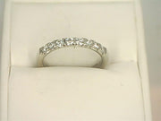 A 14K white gold ring adorned with a row of small, lab-grown diamonds is displayed on a white cushion. The 14K White Gold .4800ctw Round Cut Diamond Anniversary Band Butterfly Setting by Benchmark Rings boasts a simple yet elegant design, emphasizing the brilliance of the diamonds set in a continuous line across the upper half.