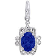 Introducing the Filigree September Stone Charm by Rembrandt Charms: a sterling silver turtle-shaped pendant with an oval-cut blue sapphire at its center. This piece showcases intricate filigree details with swirls and curves, capturing the essence of Rembrandt Charms' craftsmanship, and features a small loop at the top for easy attachment to a necklace or bracelet.