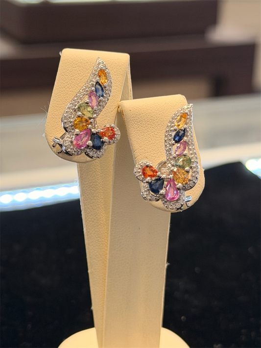 The Ryan Gems Multi Colored Sapphire Ear Climbers feature blue, orange, pink, and green sapphires set in 14k white gold, displayed on a beige jewelry stand.