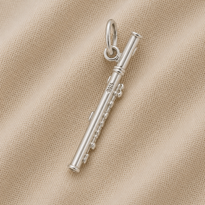 The Piccolo - Sterling Silver Charm by Rembrandt Charms, featuring a flute-shaped design with intricate chain details, is displayed on a textured beige fabric background.
