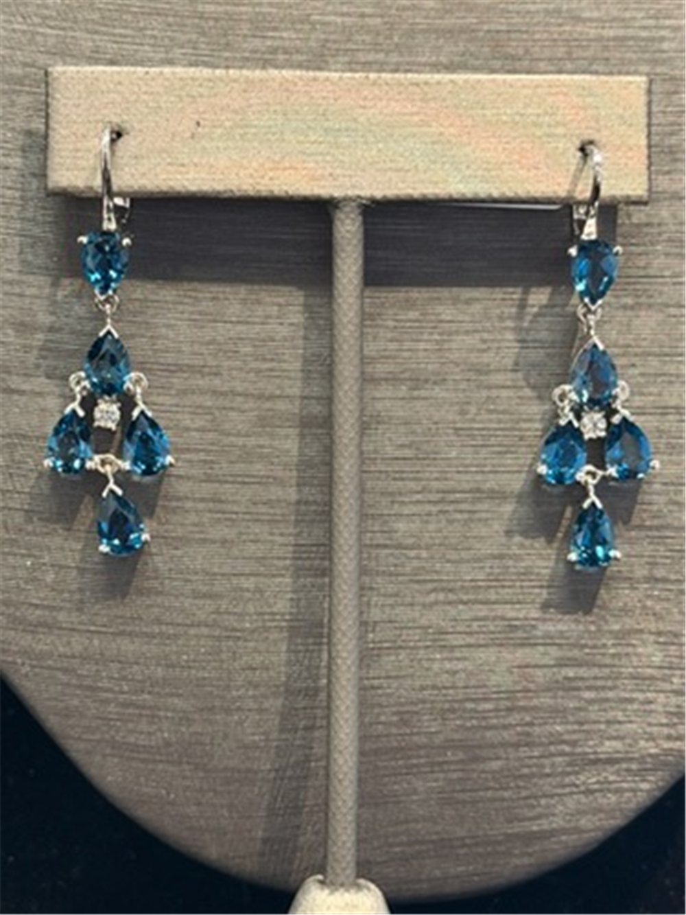 The Ryan Gems Pear Shaped London Blue Topaz Dangles feature three teardrop gems in a triangular design set in 14k white gold, accented with clear stones and displayed on a stand.
