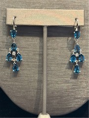 The Ryan Gems Pear Shaped London Blue Topaz Dangles feature three teardrop gems in a triangular design set in 14k white gold, accented with clear stones and displayed on a stand.