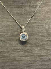 The Ryan Gems Aquamarine and Diamond Pendant in 14k white gold, featuring a round aquamarine surrounded by sparkling diamonds, is shown on a textured gray surface, highlighting its elegant beauty.