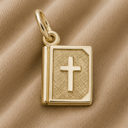 The Rembrandt Charms Bible Charm—gold plated and shaped like a book with a cross on its cover—rests elegantly on soft, textured beige fabric.